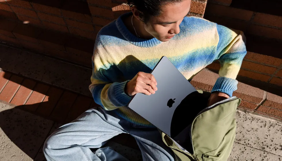 Photo en gros plan d'un étudiant souriant utilisant le MacBook Air M3 2024 dans une bibliothèque, symbolisant l'outil parfait pour la polyvalence dans les études, tel qu'expliqué dans l'article de blog.